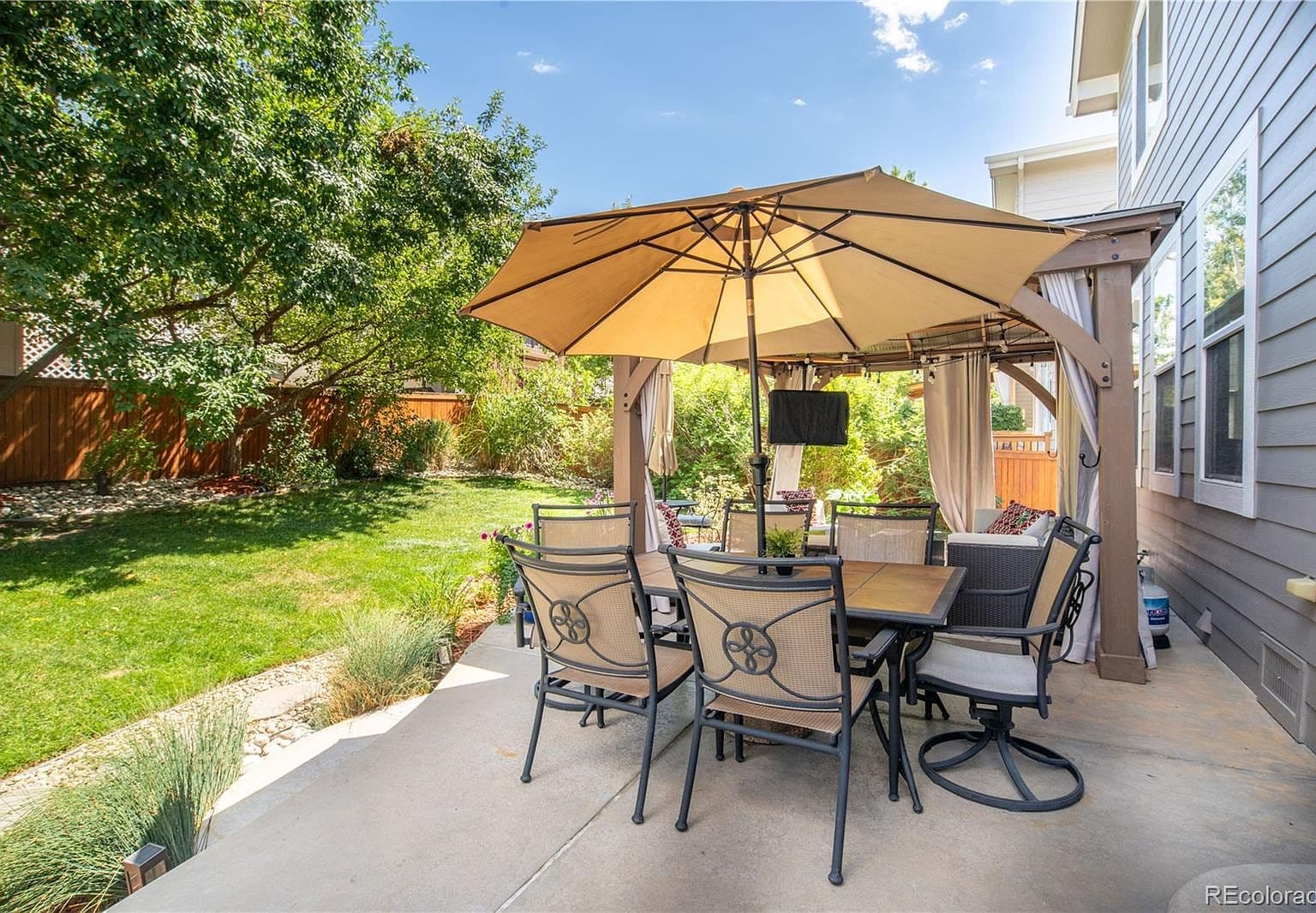 Covered patio dining beside private, green backyard oasis.