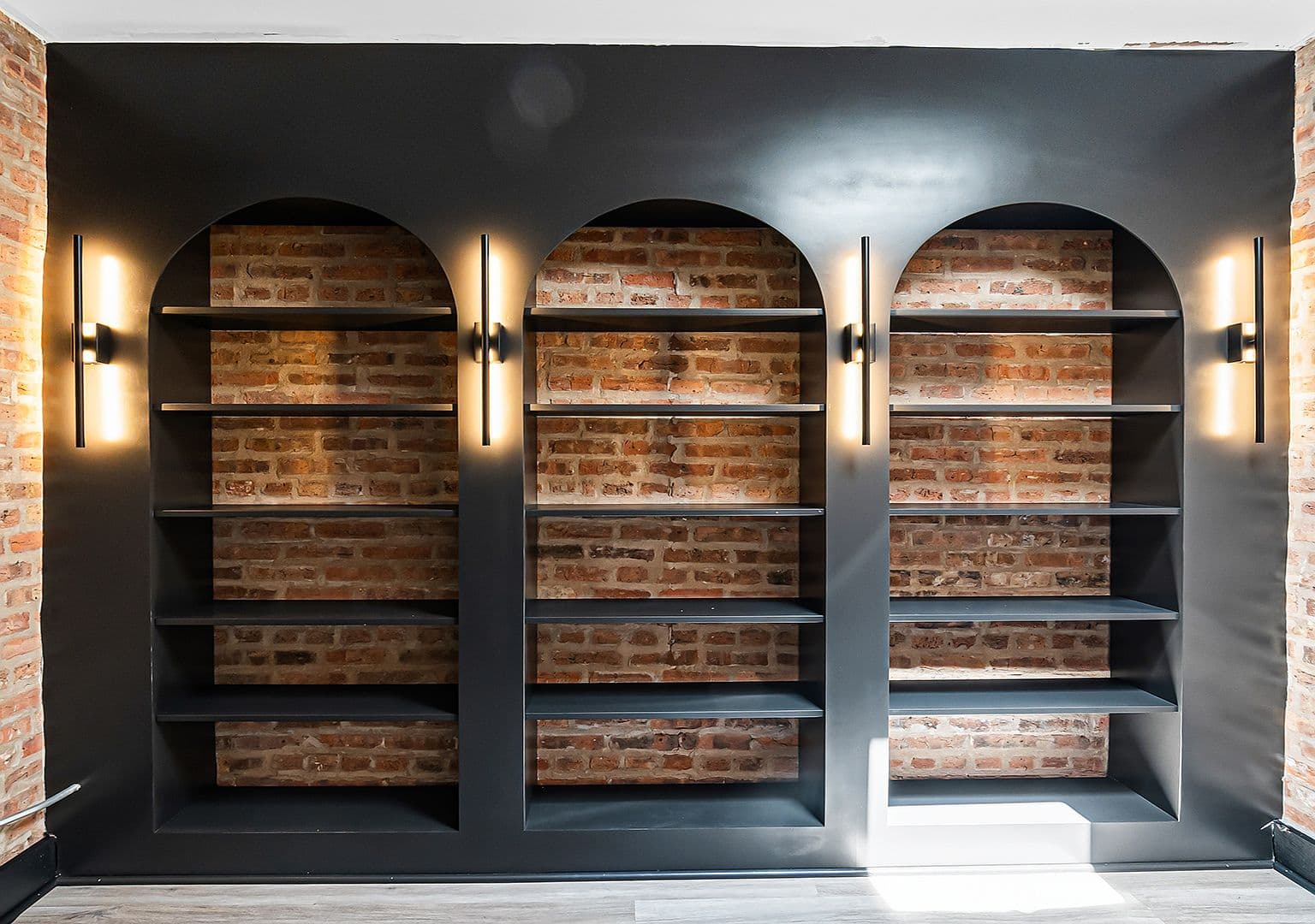 Custom arched bookcases with sconce lighting against original brick
