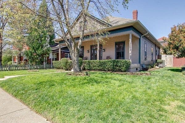 Corner-lot charm with wraparound porch and lush lawn.