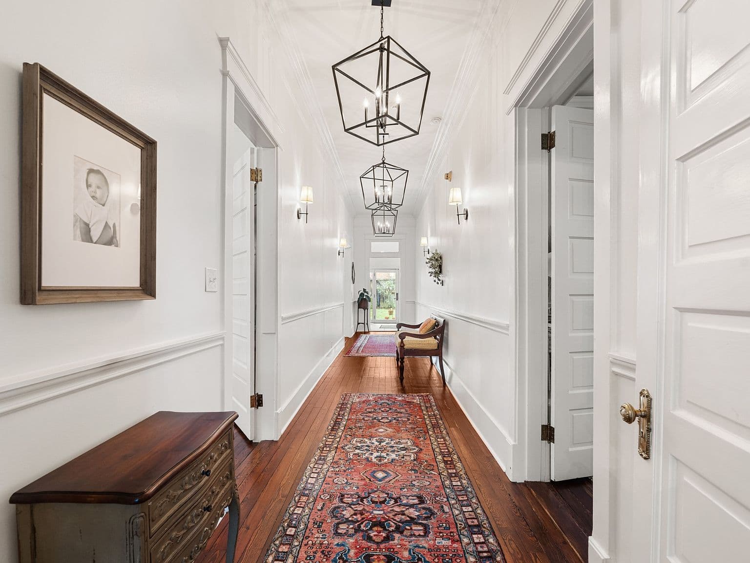 Long gallery hallway with restored floors and statement lanterns.