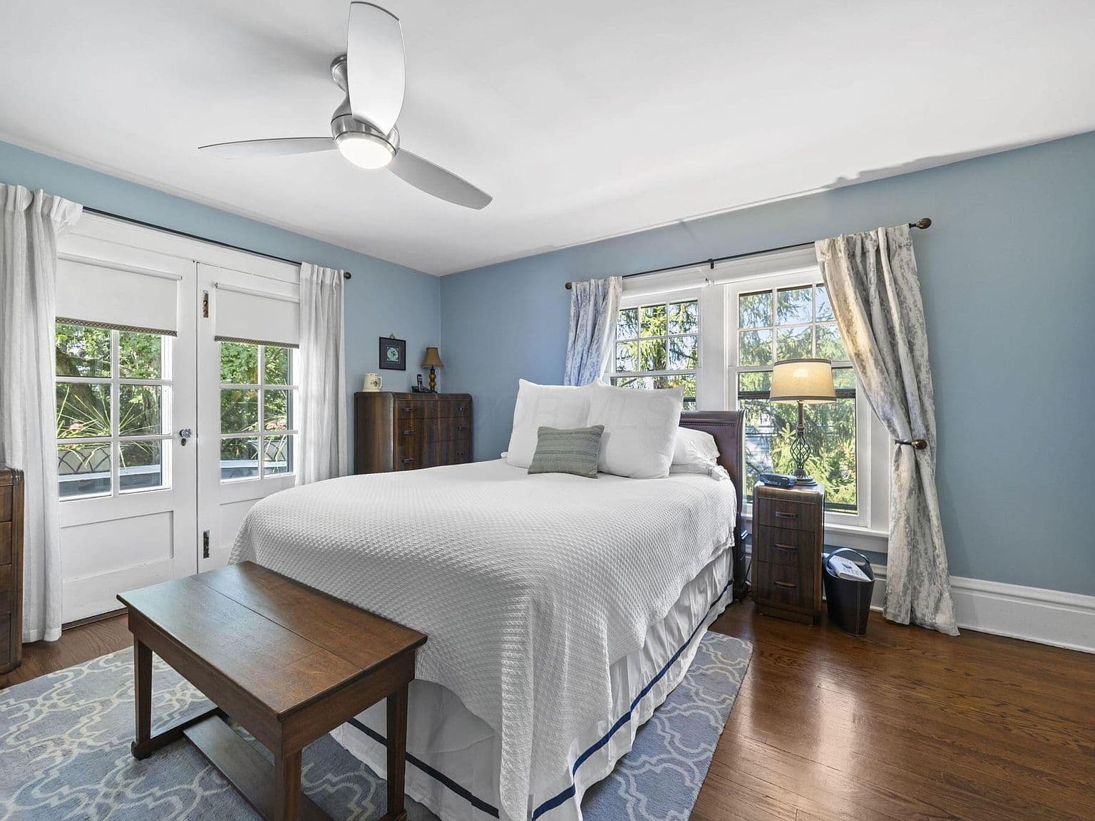 Sunlit bedroom with French doors and breezy ceiling fan.