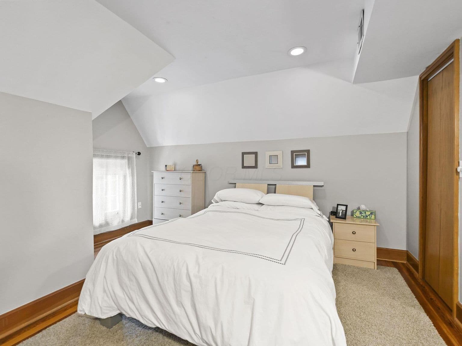Airy bedroom with vaulted ceiling and recessed lighting.