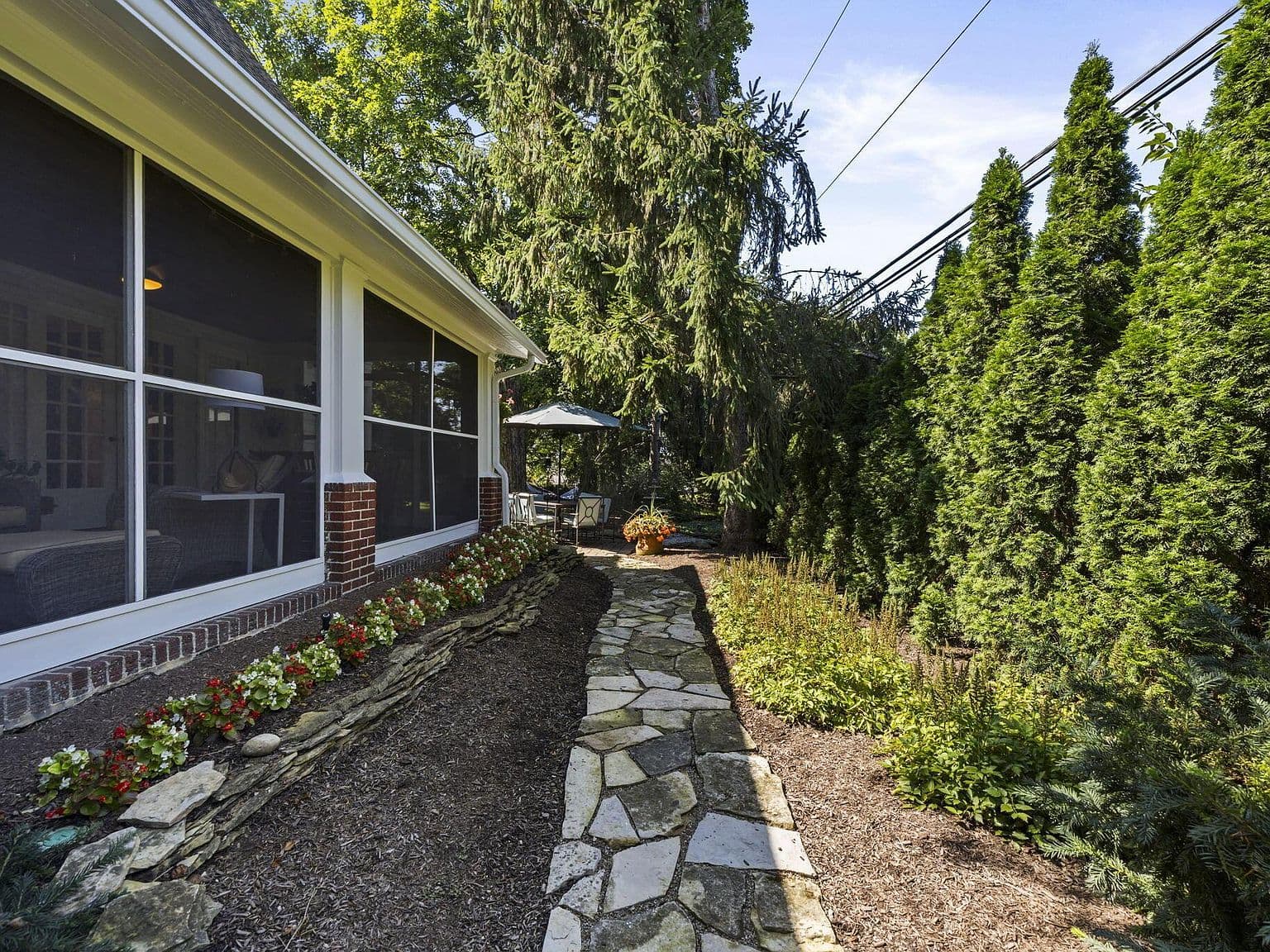 Flagstone garden path beside screened porch and privacy evergreens.