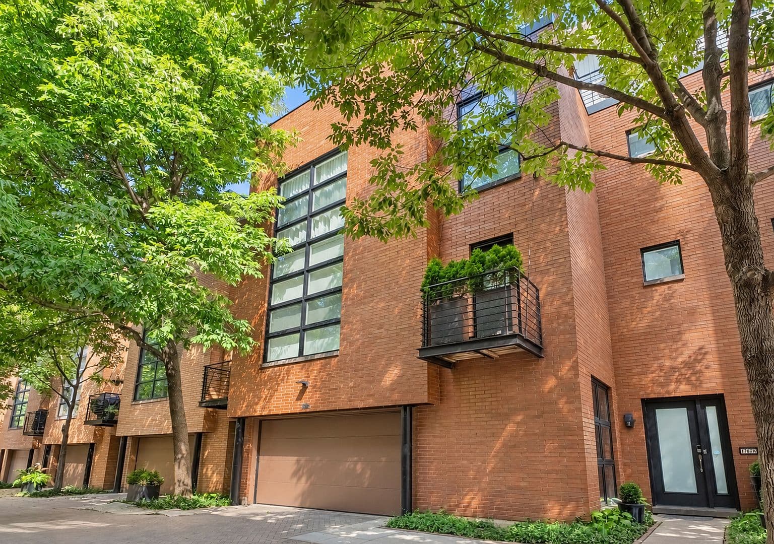 Modern brick townhome with private balconies, tree-lined street.
