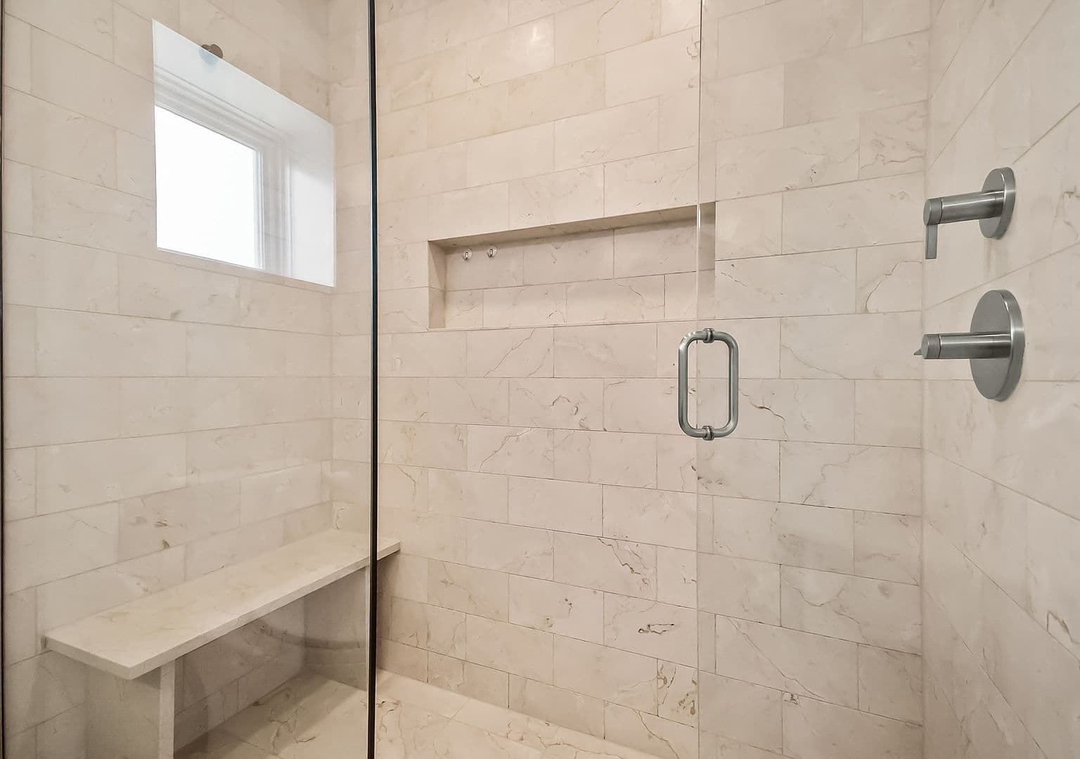 Spa-like glass shower with marble tile and bench.