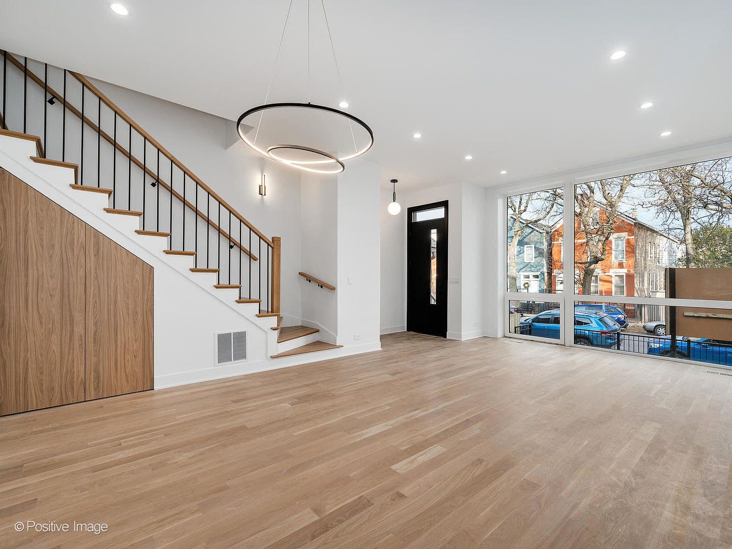 Sunlit living room with floating oak staircase and ring chandelier