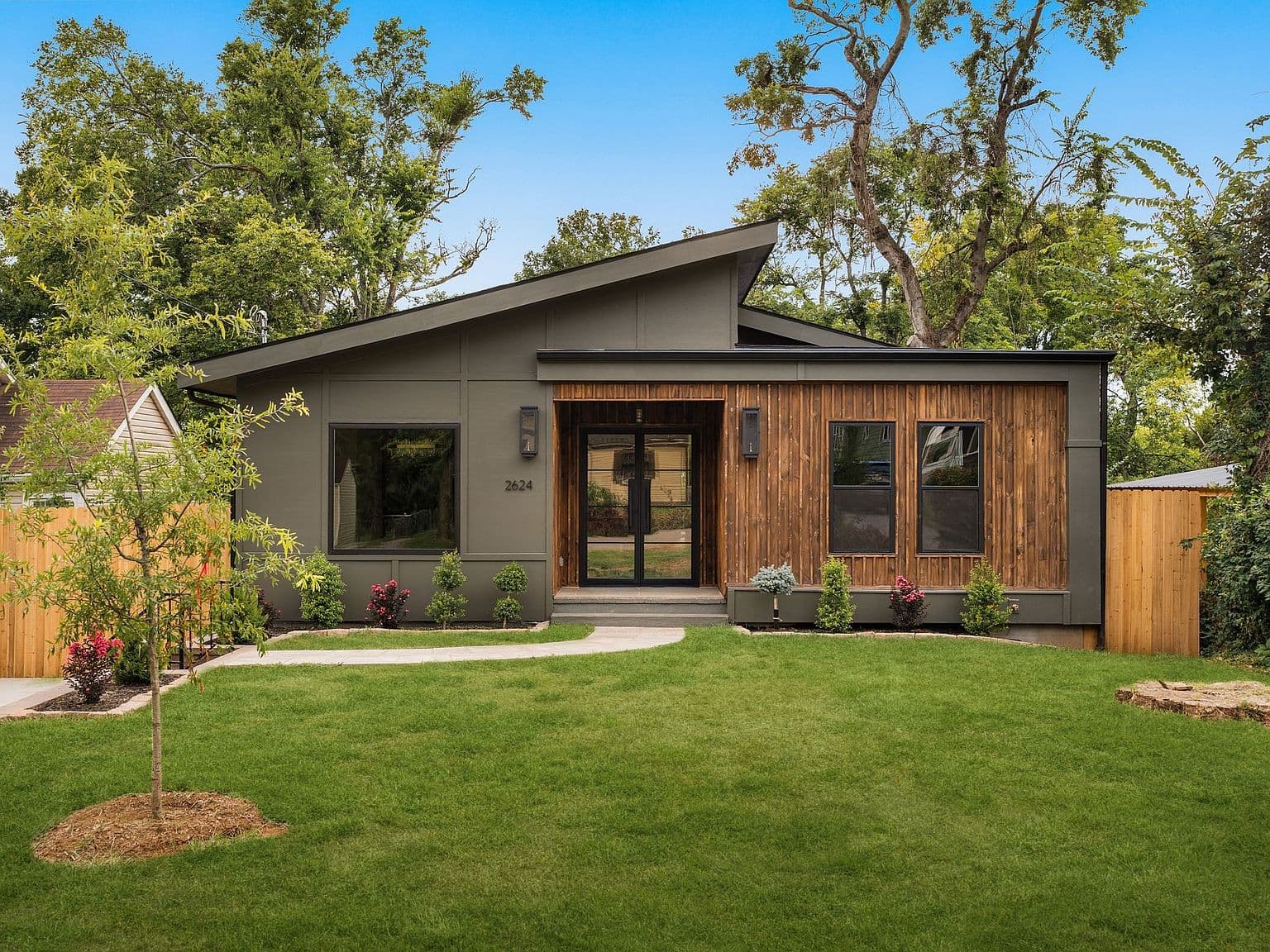 Striking modern façade on a fenced, wooded lot.