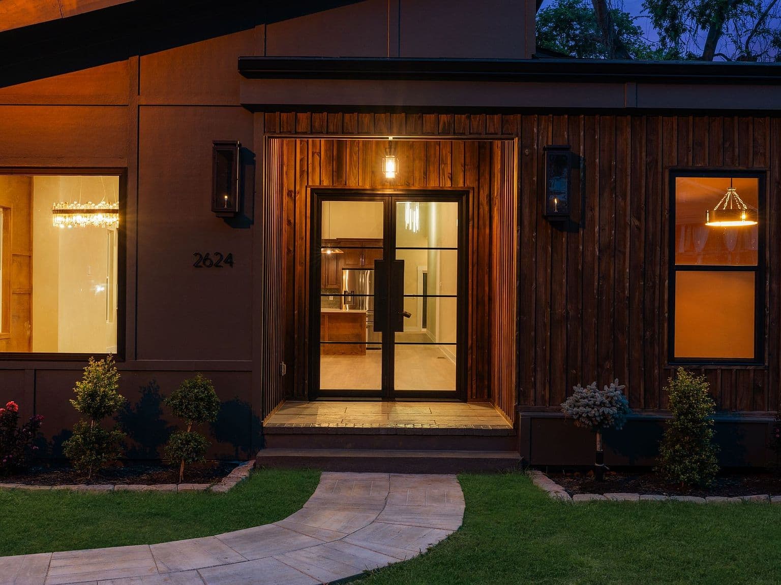 Striking modern entry with warm glow and iron doors.