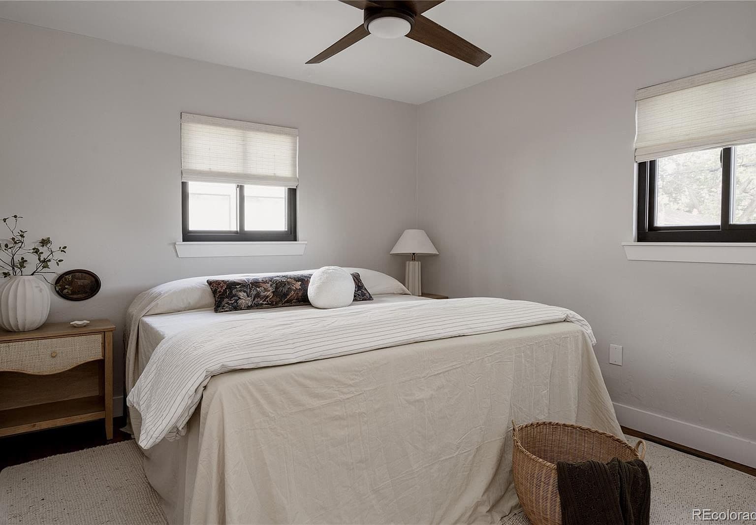 Serene bedroom enjoys two windows and a ceiling fan.
