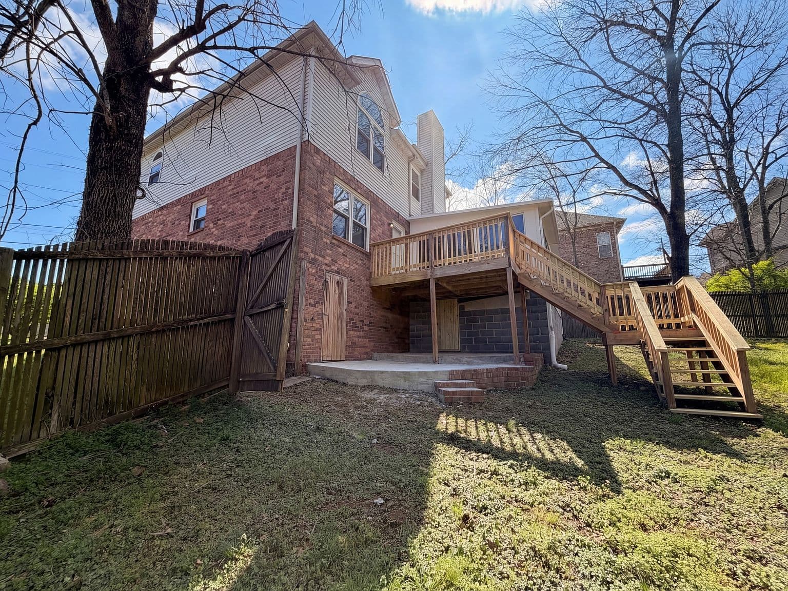 Fenced backyard with elevated deck and brick exterior.