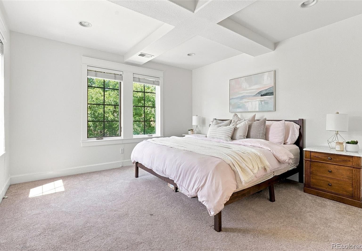 Spacious primary suite with coffered ceiling and windows.