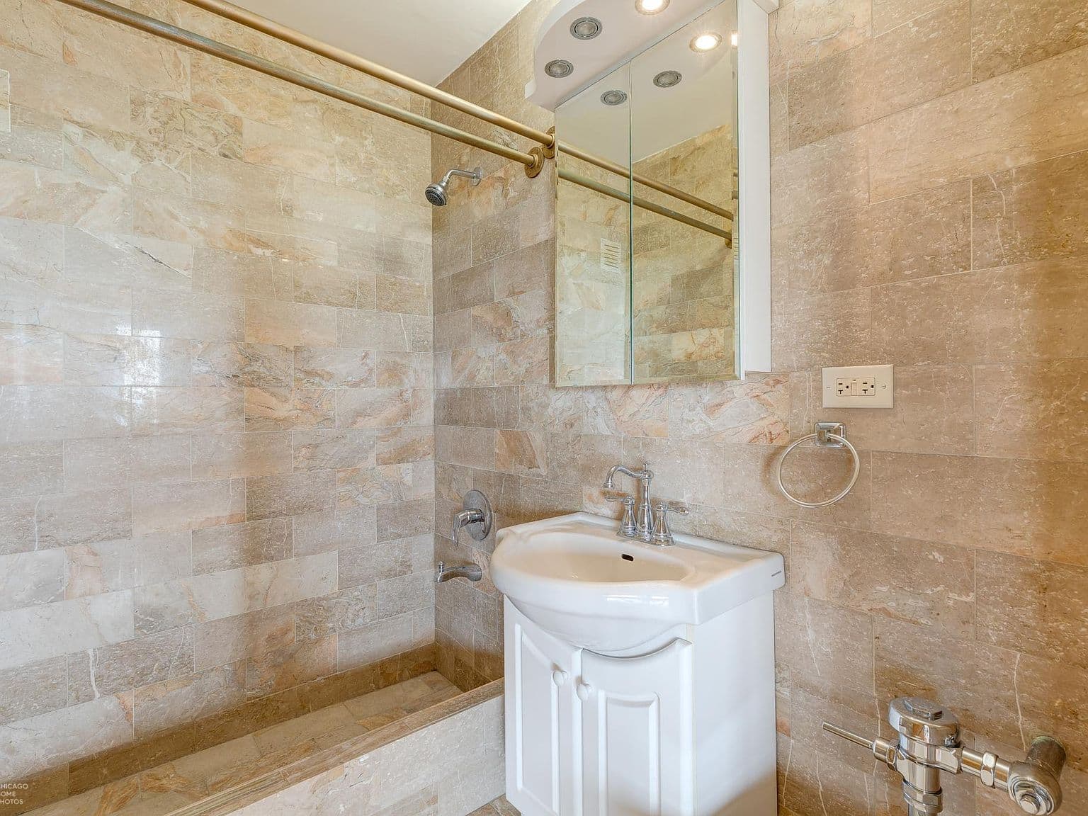 Stone-tiled bathroom features a shower-tub and mirrored vanity.