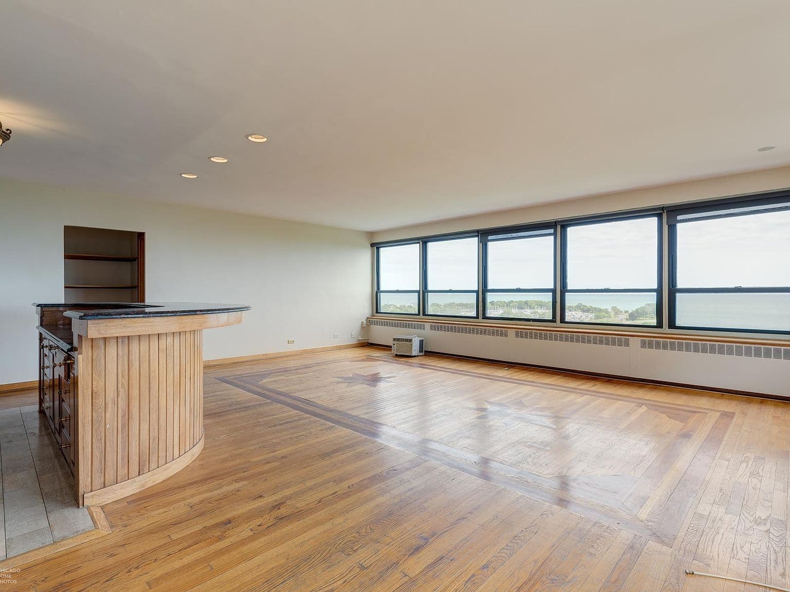 Lake-facing living room showcases expansive windows and inlaid hardwood floors.