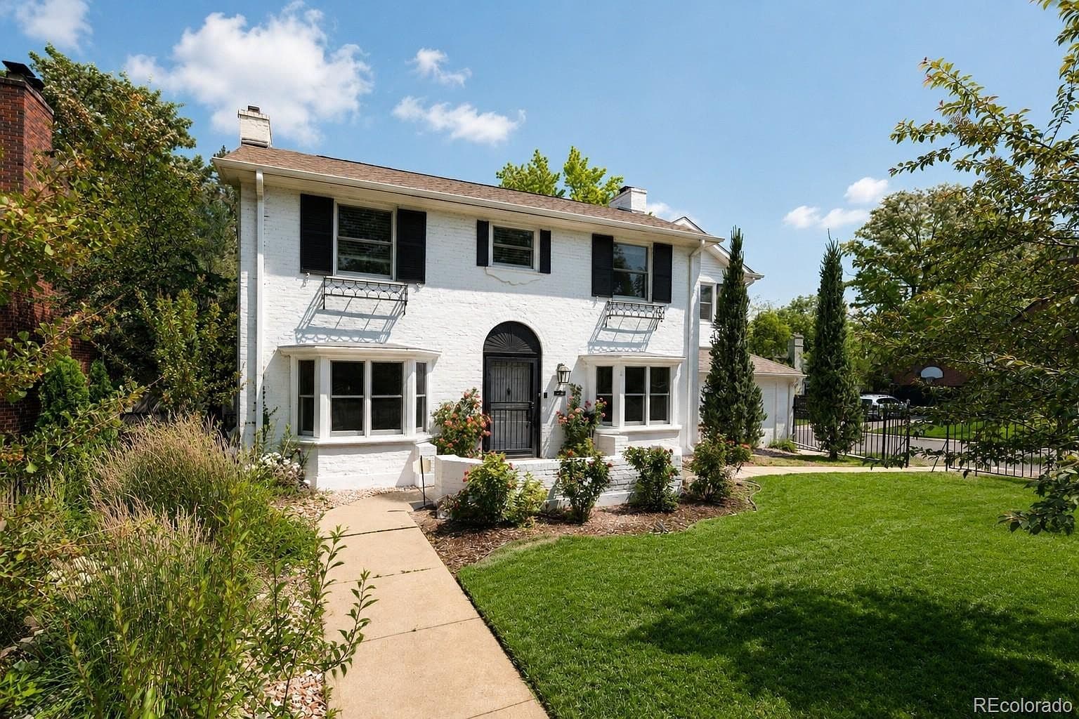 Sunlit white-brick two-story with manicured front lawn