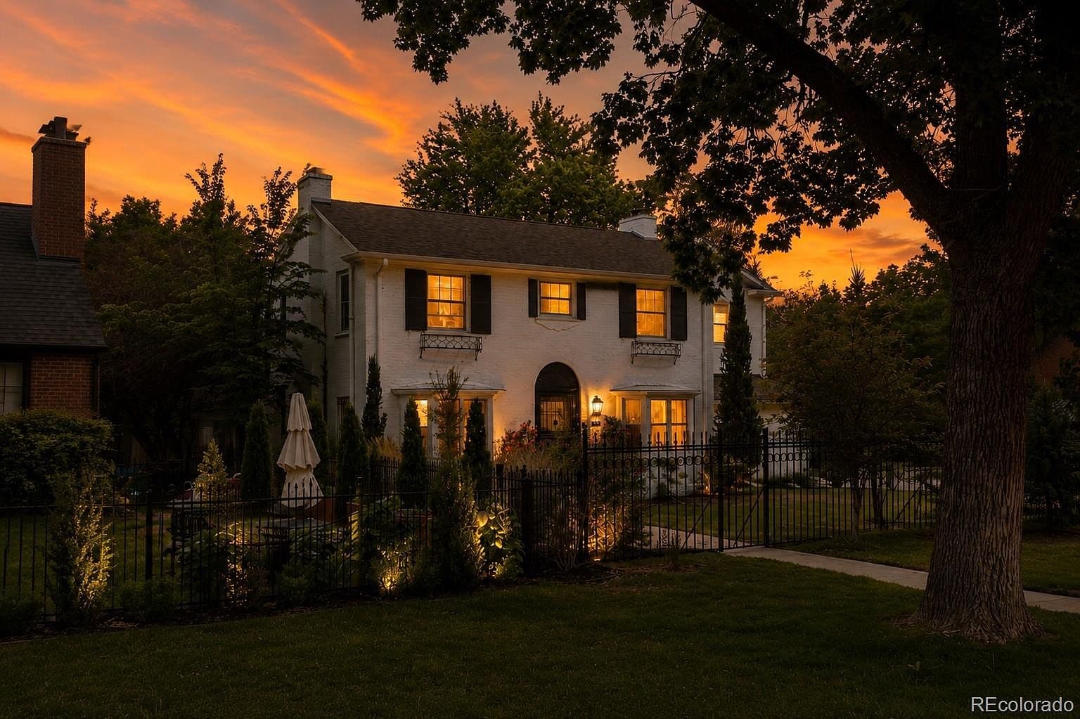 Evening facade glowing behind wrought-iron fence and landscape lighting